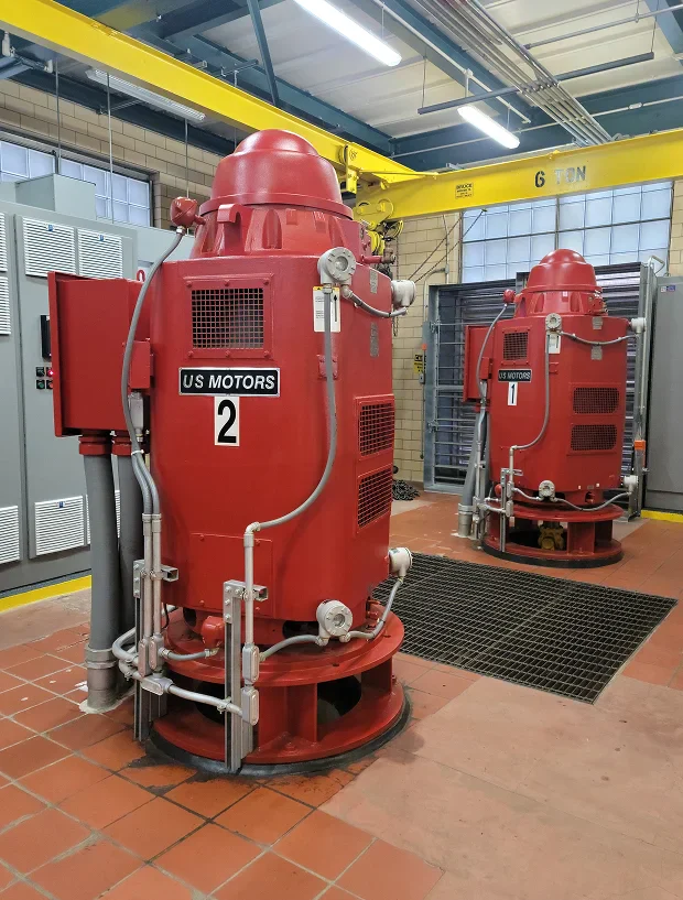 Two large red electric motors labeled 'US MOTORS 1' and 'US MOTORS 2' are set against a tiled industrial backdrop