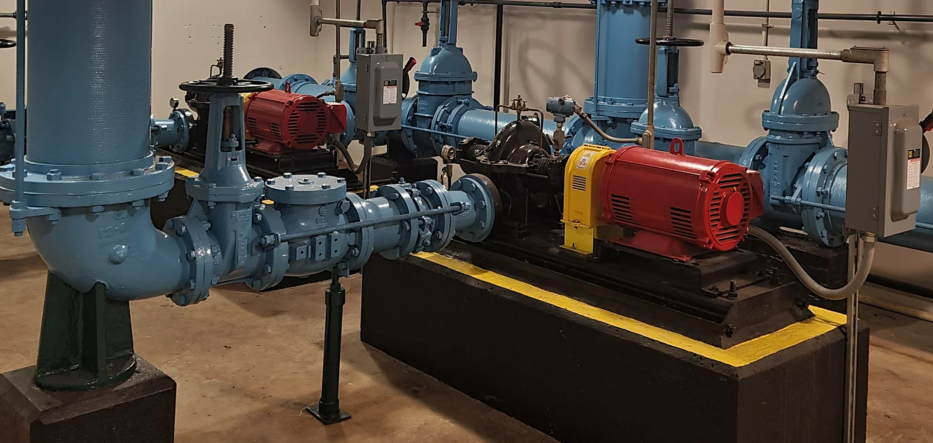 Pumping station interior showcasing blue valves and pipes, with red and yellow electric motors mounted on a black platform