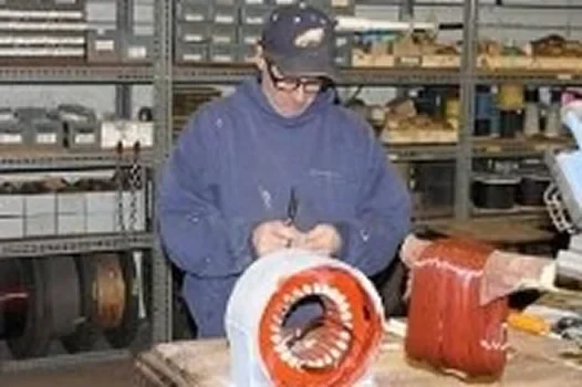 A technician repairs electric motor components on a workbench, surrounded by tools and parts in a workshop