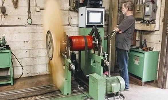 A technician monitors a rotating machine in a workshop, with a computer displaying data about the device's performance and speed