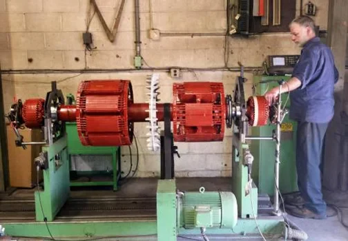 A technician operates machinery to test electric motors, featuring red motor components mounted on a green testing apparatus