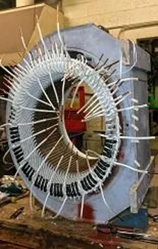 A cylindrical electrical coil assembly with multiple insulated wires wrapped around a metal core, set on a workshop bench