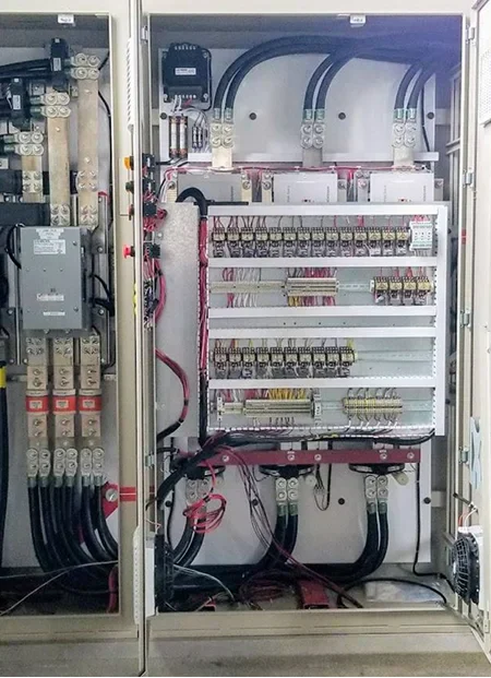 Interior of an electrical panel with multiple circuit breakers, wires, and control modules neatly organized and connected
