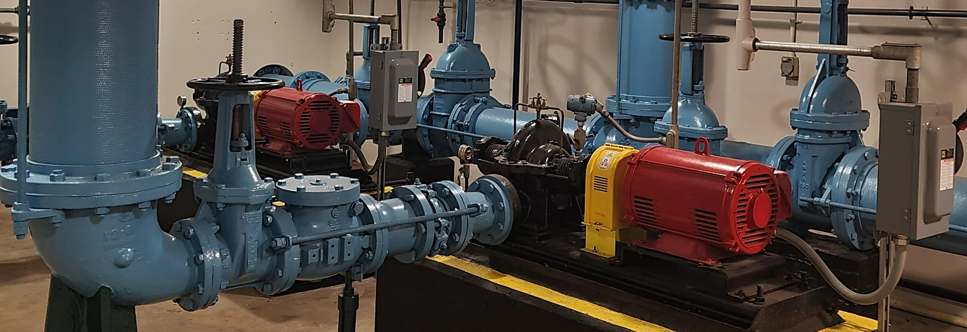 Pumping station interior showcasing blue valves and pipes, with red and yellow electric motors mounted on a black platform